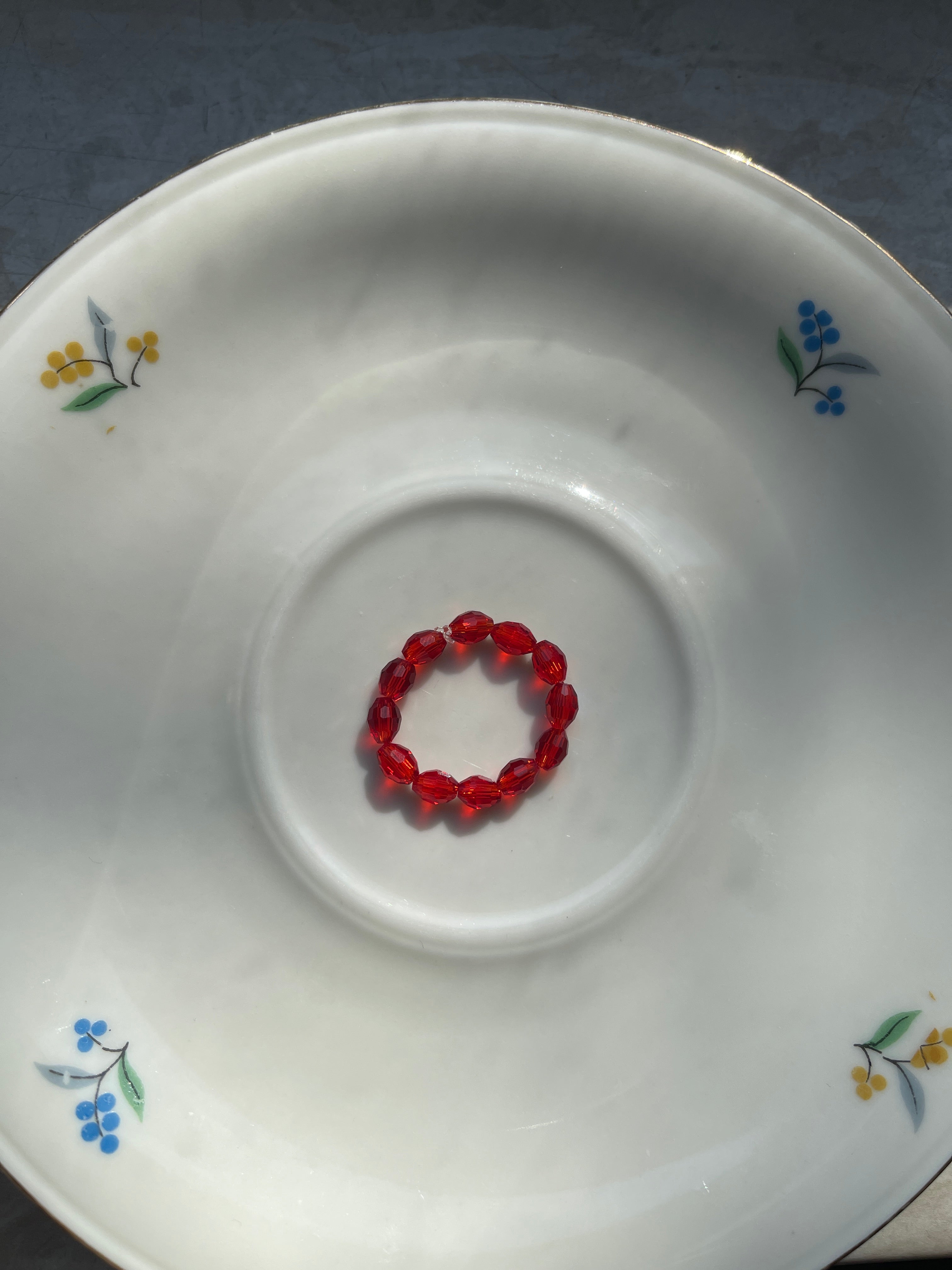 Elastischer Ring aus Perlen rot als Produktfotografie auf einem Teller
