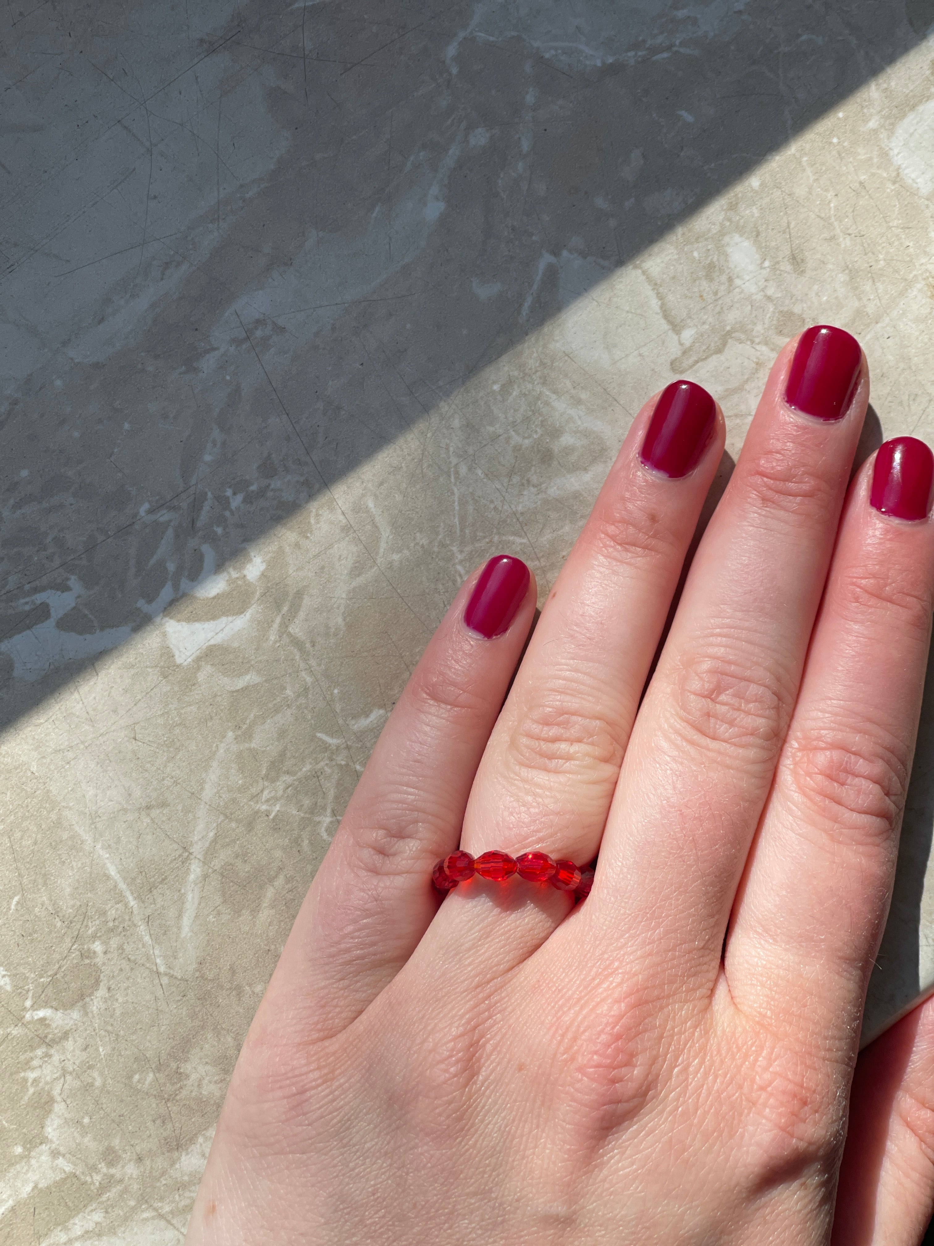 Elastischer Ring aus Perlen rot an der Hand gezeigt