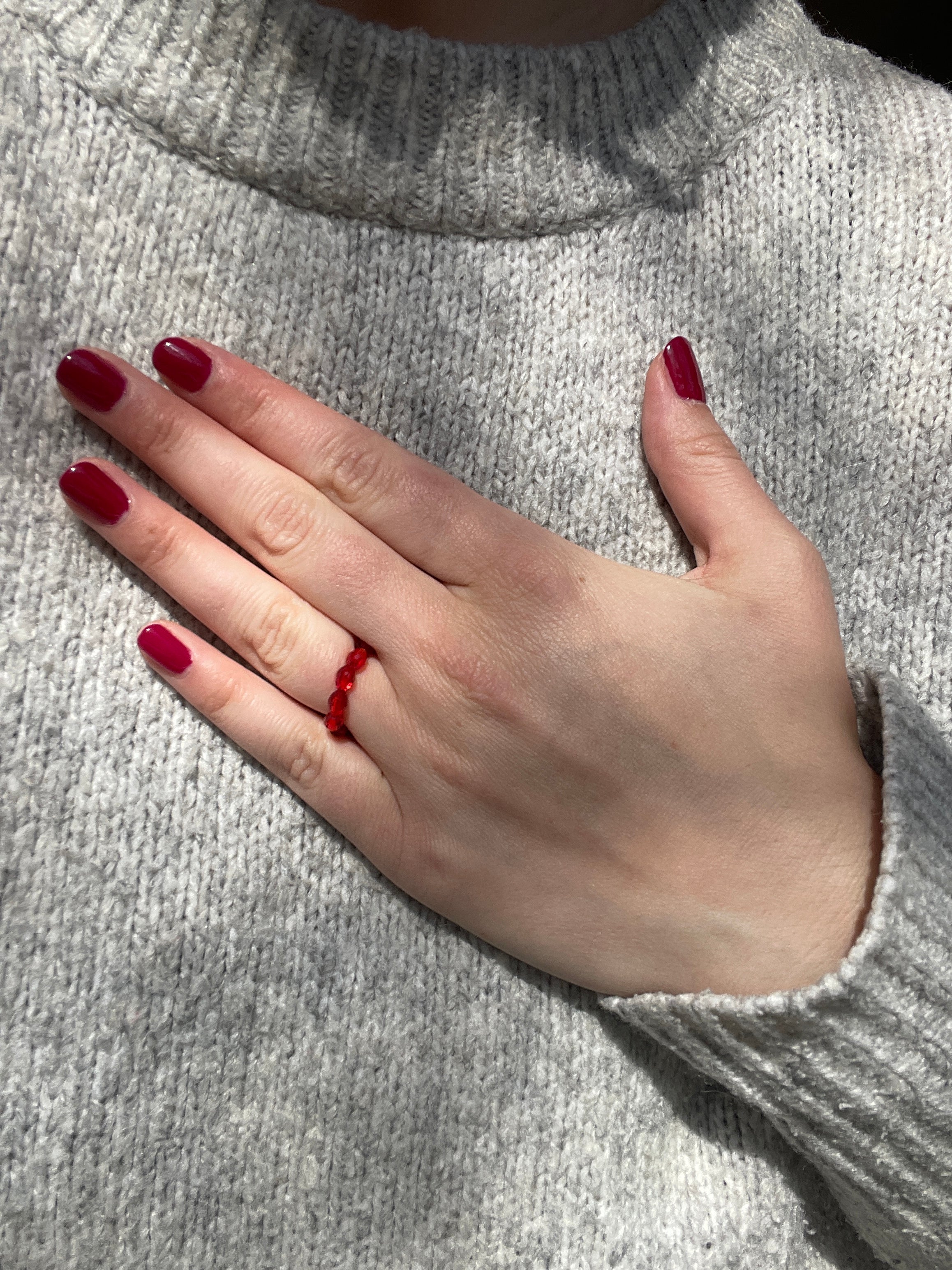 Elastischer Ring aus Perlen rot an der Hand gezeigt