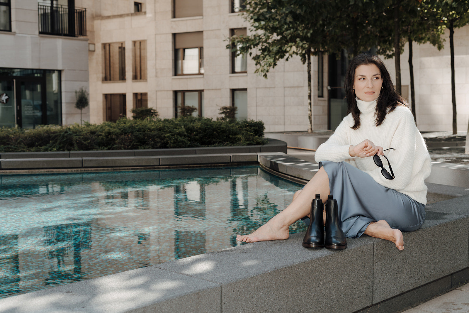 Model im Herbstlook für große Frauen sitzend am Wasser mit Sonnenbrille davor Chelsea Boots Damenschuhe in Übergröße von Kathis shoes